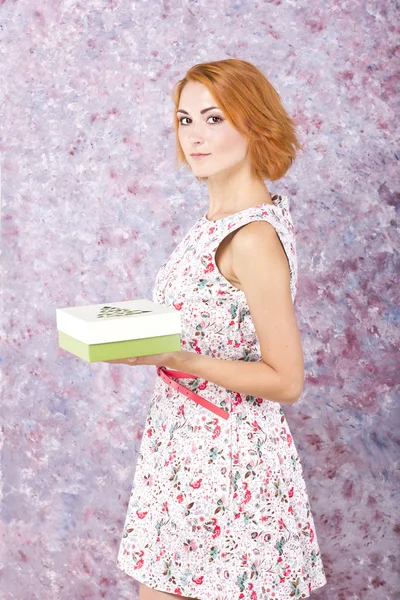 Charming young girl holding a gift box. Bright oil background. Hair style. Red short hair