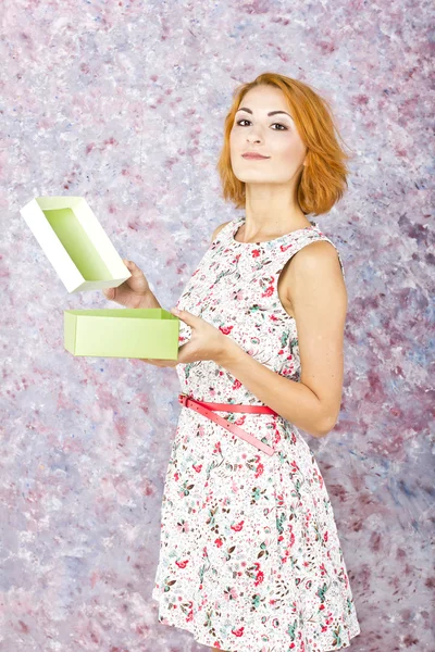 Charming young girl holding a gift box. Bright oil background. Hair style. Red short hair