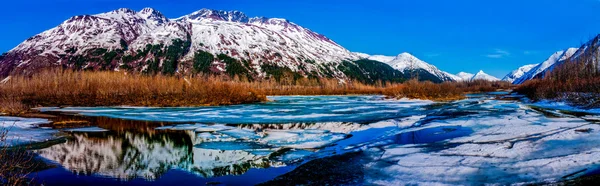 A Colorful Panorama of a Partially Frozen Lake with Mountain Range Reflected in the Great Alaskan Wilderness.