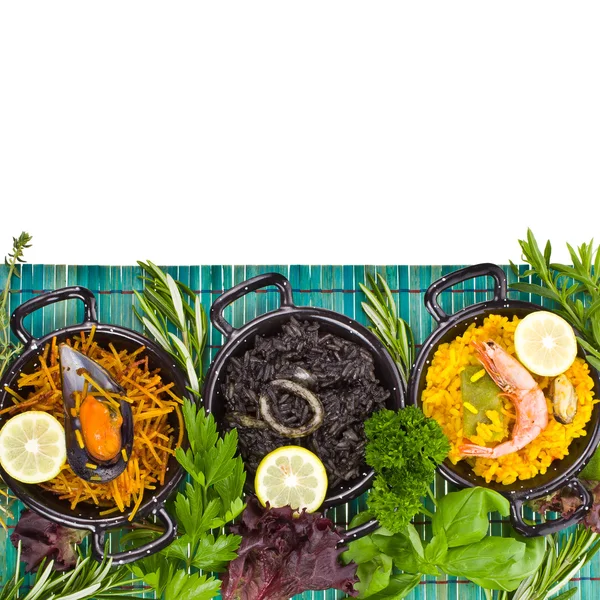 Spanish Mediterranean sea food - black rice, paella, noodles in a typical small pan on the blue mat isolated on white background