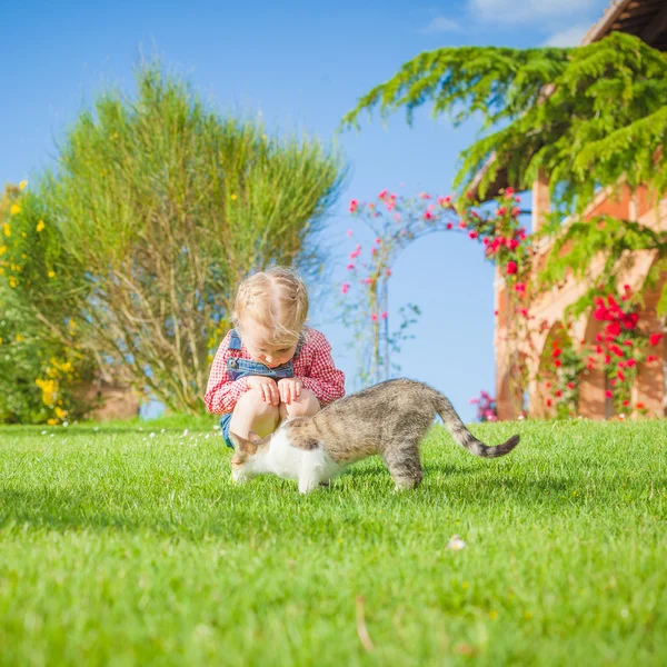 Little girl plays with a cat on a green blade of grass