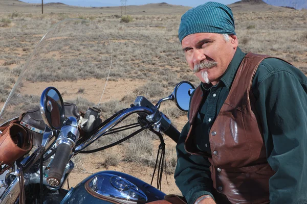 Handsome older man leaning against large motorcycle outdoors in brown desert