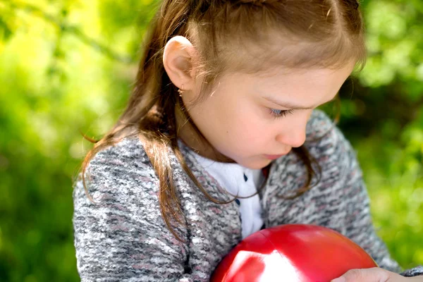 Outdoor portrait of sad little girl holding a red ball in her ha