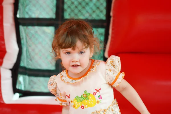 Little pretty happy girl in dress plays in red bouncy castle