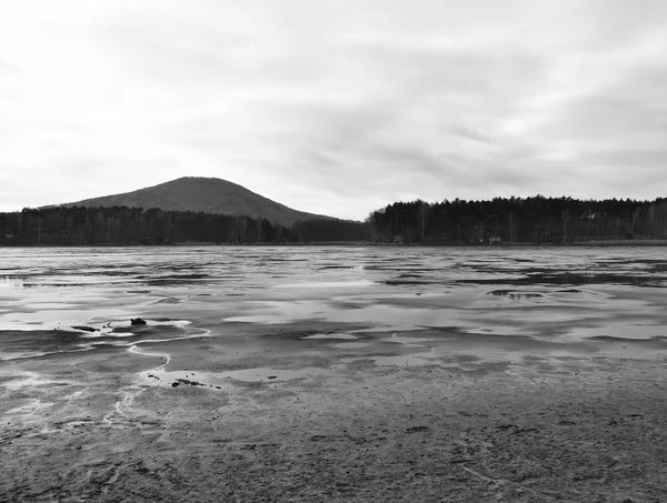 Sad view over empty pond to hill and forest on oposite bank. Autumn melancholic atmosphere. Black and white photo.