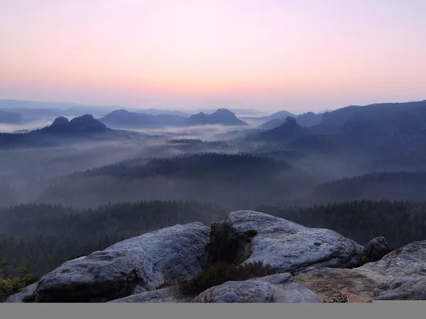 Unrise in a beautiful mountain of Bohemian-Saxony Switzerland. Sandstone peaks and hills increased from foggy background, the fog is orange due to sun rays.