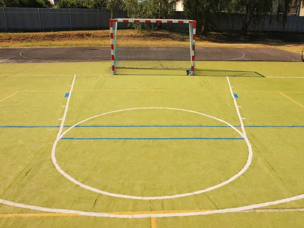 Empty outdoor hanball playground, plastic light green surface on ground and white blue bounds lines.