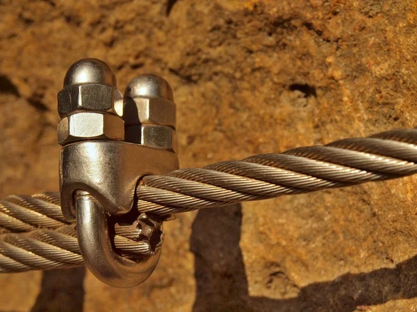 Detail of chrome screws snap hooks and grommets at and of rope. Iron twisted rope fixed together by screws snap hooks. Detail of rope end anchored at sandstone rock