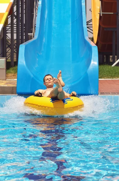 Men go down from water slide to swimming pool in aqua park.