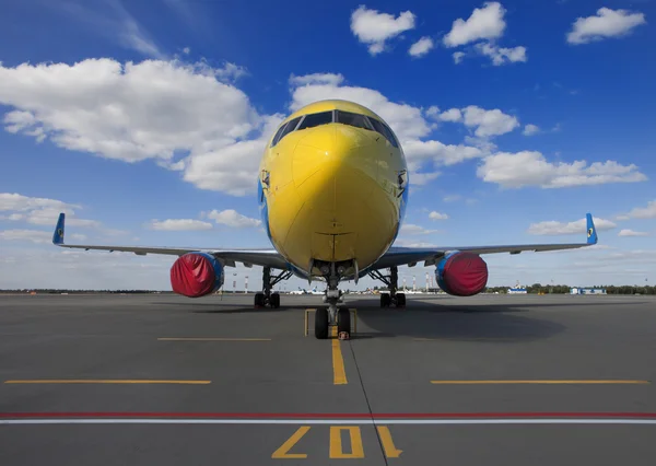 Yellow commercial airplane with covered turbines parked on an airfield