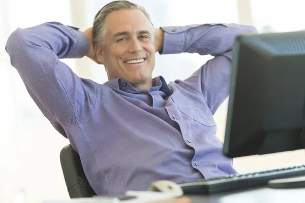 Businessman Sitting With Hands Behind Head At Office Desk