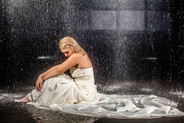 Bride sitting under rain in wet dress