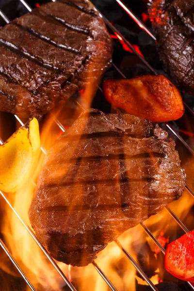 Beef steak on a barbecue grill with flames with vegetables