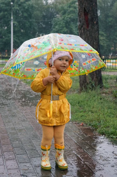 Two-year-old girl in a yellow raincoat hiding from the rain unde