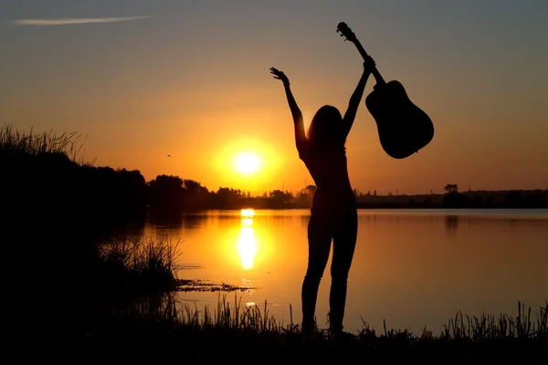 Silhouette of a happy girl with a guitar by the river