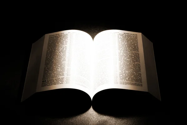 Open old Bible on a table with light shed on it