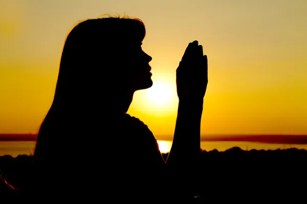 Silhouette of a girl raises her hands to God