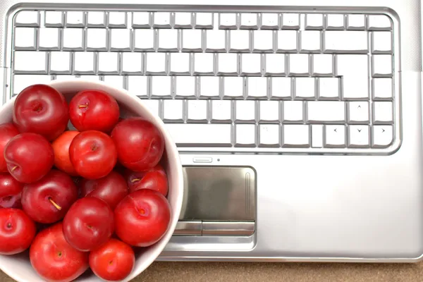 Laptop, plums and shells on wood