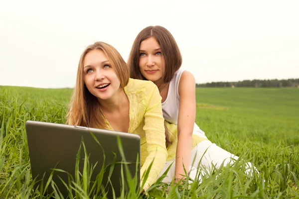 Two beautiful happy girls using a laptop in grass area