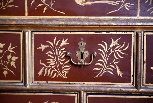 Old metal keyhole crown on an old chest of drawers painted with gold floral ornament