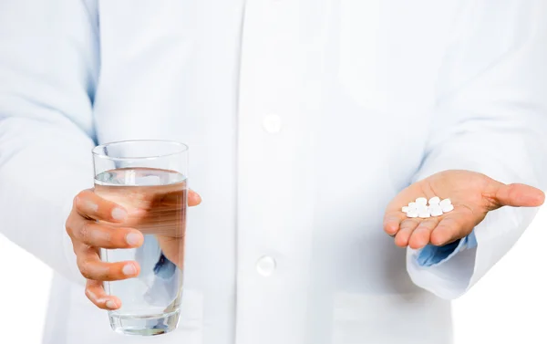 Doctor holding glass of water in one hand and white pills in the other