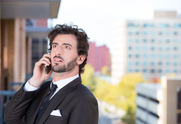 Closeup portrait of a handsome young, happy business man talking on a cell phone relaxed on a balcony of his apartment isolated on a city background