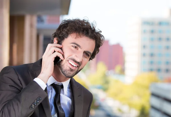 Closeup portrait of a handsome young, smiling business man talking on a cell phone relaxed on a balcony of his apartment isolated on a city background