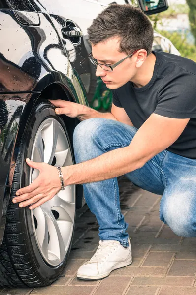 Young man with glasses inspecting a tire of a luxury car before a second hand trade