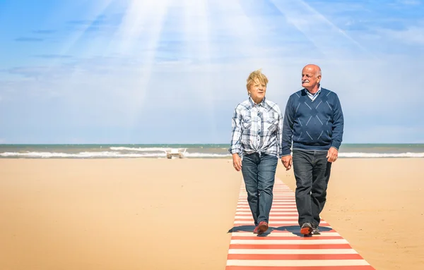 Happy senior couple in love walking hand in hand at the beach - Healthy and joyful elderly lifestyle with man and her wife spending time together outdoors in a sunny day