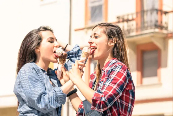 Young women best friends sharing an ice-cream during a sunny day walking around in the city center - Concept of carefree friendship during spring enjoying the upcoming summer