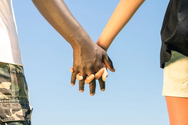 Multiracial couple walking hand in hand against a blue sky - Concept of multi ethnic love over social barriers