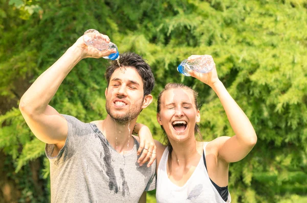 Sporty couple refreshing with cold water after run training in the park - Sport fitness young happy models taking a break after jogging in the nature