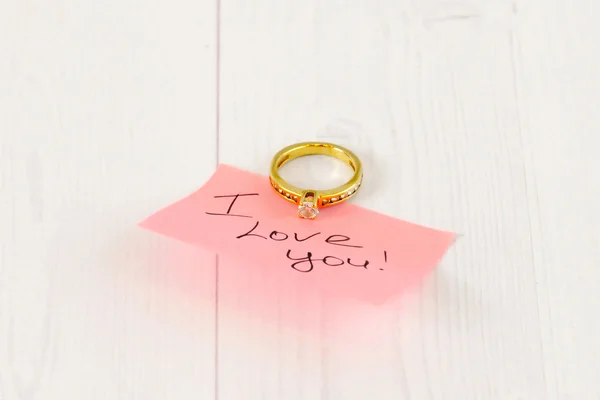 Gold ring with pink sticker on white wood
