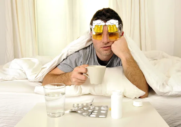 Man with headache and hangover in bed with tablets