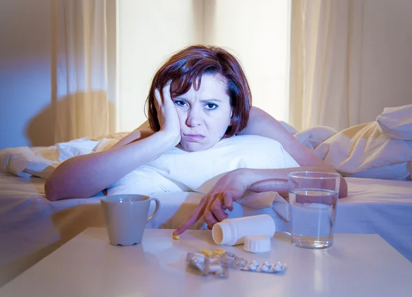 Red haired woman sick in bed with medicine