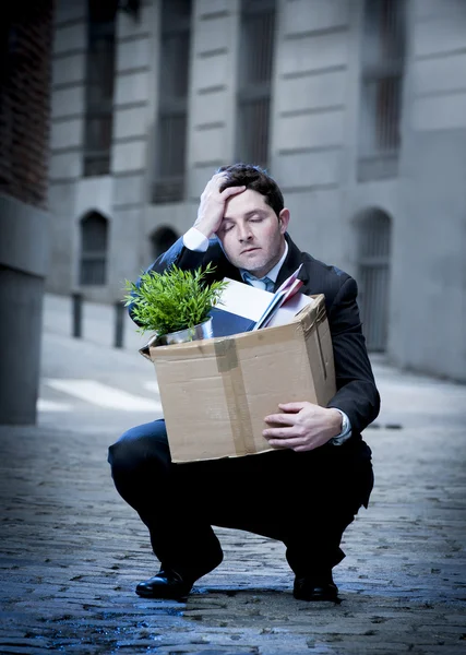 Frustrated business man on edgy street fired from job carrying cardboard box looking desperate and in stress