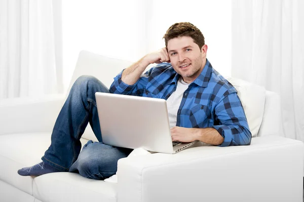 Attractive man working with computer sitting on couch at home