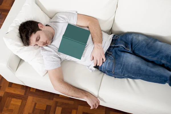 Tired young man sleeping on couch with book on lap