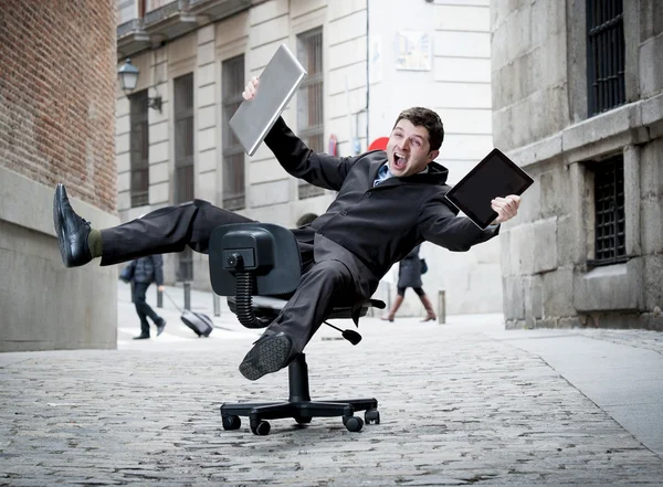 business man rolling downhill on chair with computer and tablet