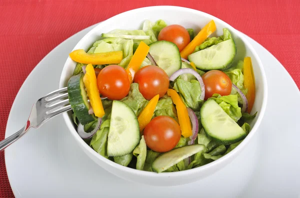 Fork with cherry tomato, carrot and cucumber in healthy salad bowl