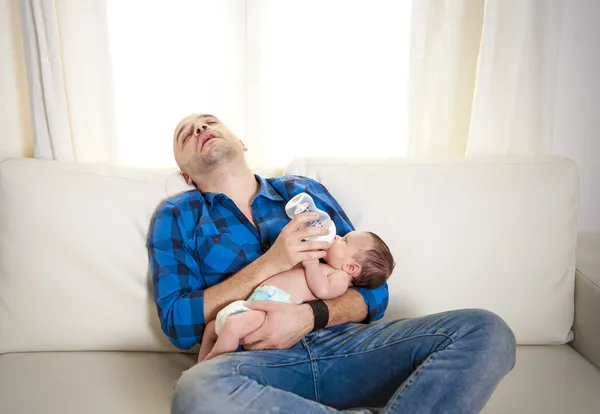 New father alseep while feeding his newborn baby