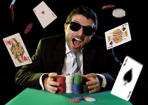 Happy young attractive man grabbing poker chips after winning bet gambling