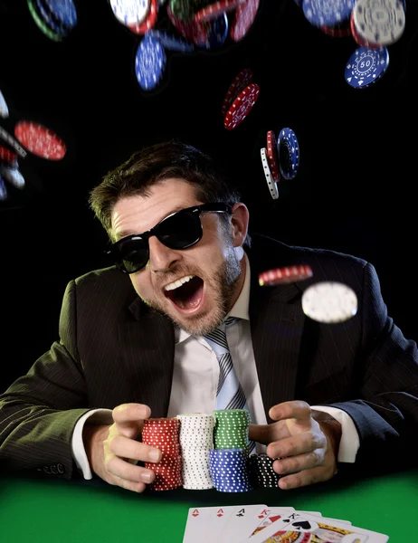 Happy young attractive man grabbing poker chips after winning bet gambling