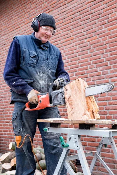 Elderly man working with chain saw on tree trunk
