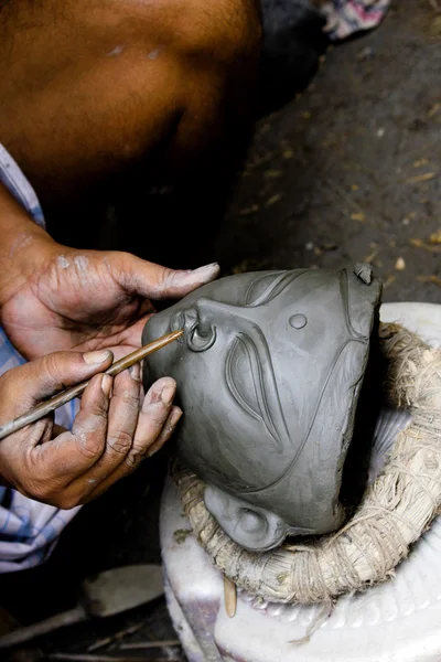 An artisan creates clay head of goddess Durga