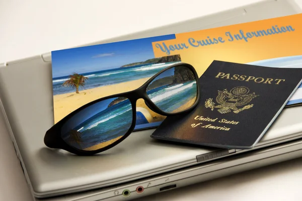 Sunglasses reflect an exotic Caribbean beachwith international passport, cruise information and travel laptop