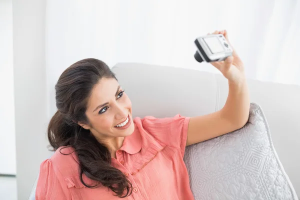 Brunette sitting on her sofa taking a picture of herself