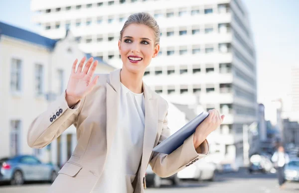 Smiling gorgeous businesswoman holding tablet pc waving