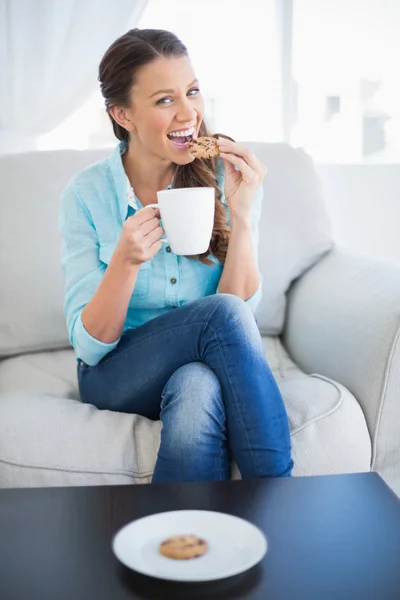 Happy woman holding cup of coffee eating cookie