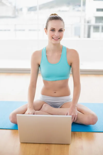 Sporty happy woman sitting cross-legged in front of laptop